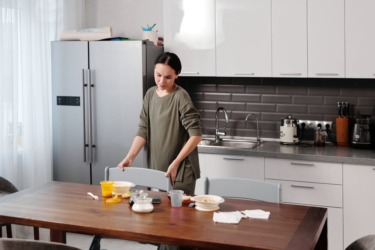 A woman tidying up the kitchen, organizing dishes and cleaning the table in a cozy home environment.
